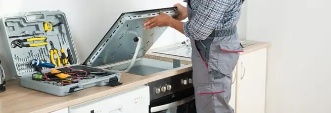 Cooktop repair technician lifting a built-in stovetop for service in Mesa, AZ