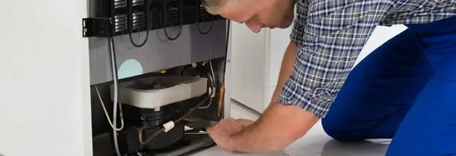Refrigerator repair technician servicing the compressor and condenser area in Mesa, AZ