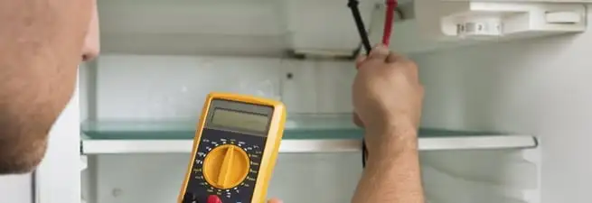 Refrigerator repair technician testing electrical components with a multimeter in Mesa, AZ