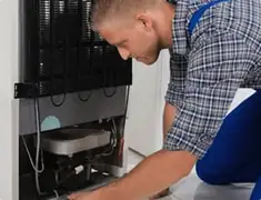 Refrigerator repair technician servicing the compressor and condenser area in Mesa, AZ